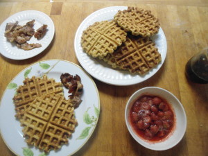 Breakfast fixings, barley flour waffles, strawberries, bacon and maple syrup